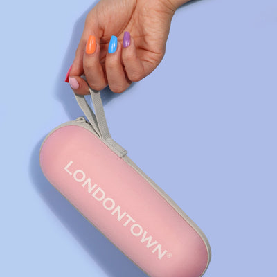 A hand with multicolored nails holds a pink Signature Mini Umbrella labeled "LONDONTOWN," a perfect travel companion against a light blue background.