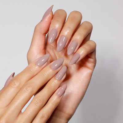 Hands with long, almond-shaped nails painted in LONDONTOWN's Do Not Disturb, a glossy taupe polish with subtle mauve undertones, against a plain background.