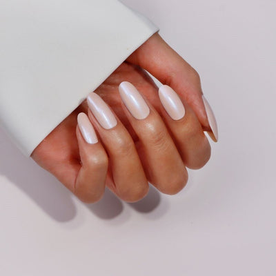 A hand with long, smooth, light-colored nails features LONDONTOWN's Starry Chrome Duo polish, which seems to transform from crème to chrome against a plain background.