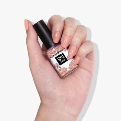 A hand holds a LONDONTOWN Rose Latte Gel Color nail polish bottle, with nails painted in a matching warm pink shade.