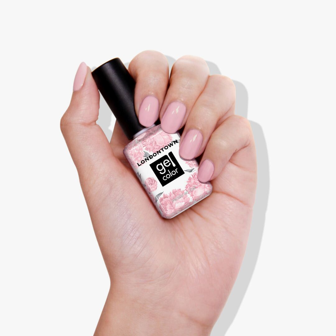 A hand holds a bottle of LONDONTOWN's Magnolia Haze gel color nail polish, flaunting nails painted in a sheer petal pink. This versatile shade is perfect for any occasion.