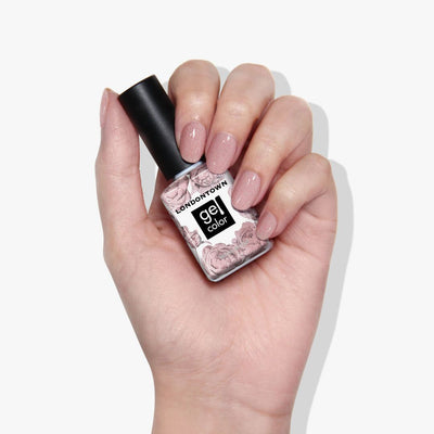 A hand gracefully holds a bottle of LONDONTOWN's "Champagne in Bed" gel nail polish, nails adorned in a matching shimmery mauve with subtle sparkle.