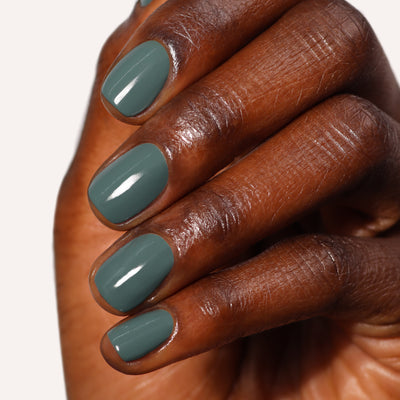 A hand with medium-dark skin tone displays nails painted in a glossy, sumptuous olive green color, Velvet Drapes by LONDONTOWN, against a plain background.