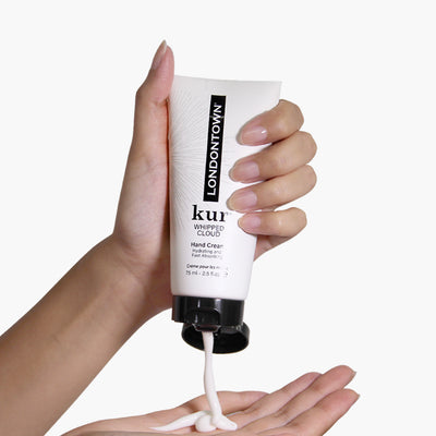 A hand applying LONDONTOWN Whipped Cloud Hand Cream from a tube onto an open palm.