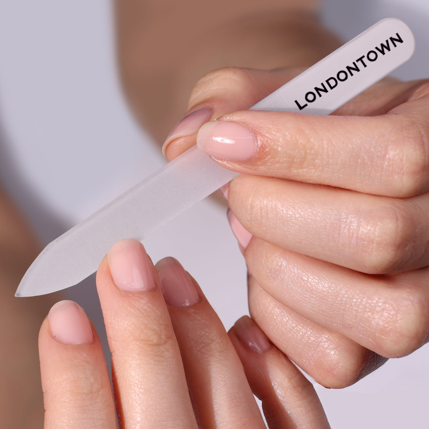 Hands effortlessly filing fingernails with LONDONTOWN's translucent, damage-free Glass Nail File - Clear (Professional).