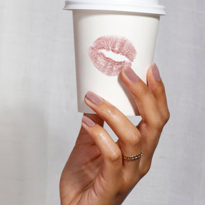 A hand with pink nails holds a LONDONTOWN "Do Not Disturb" white coffee cup featuring a lipstick kiss mark, making a bold statement.