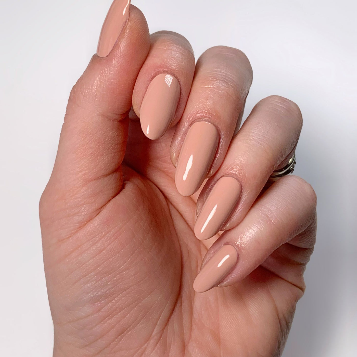 A hand with neatly manicured long nails painted in LONDONTOWN's Rose Latte, a glossy pink beige hue, set against a warm white background.