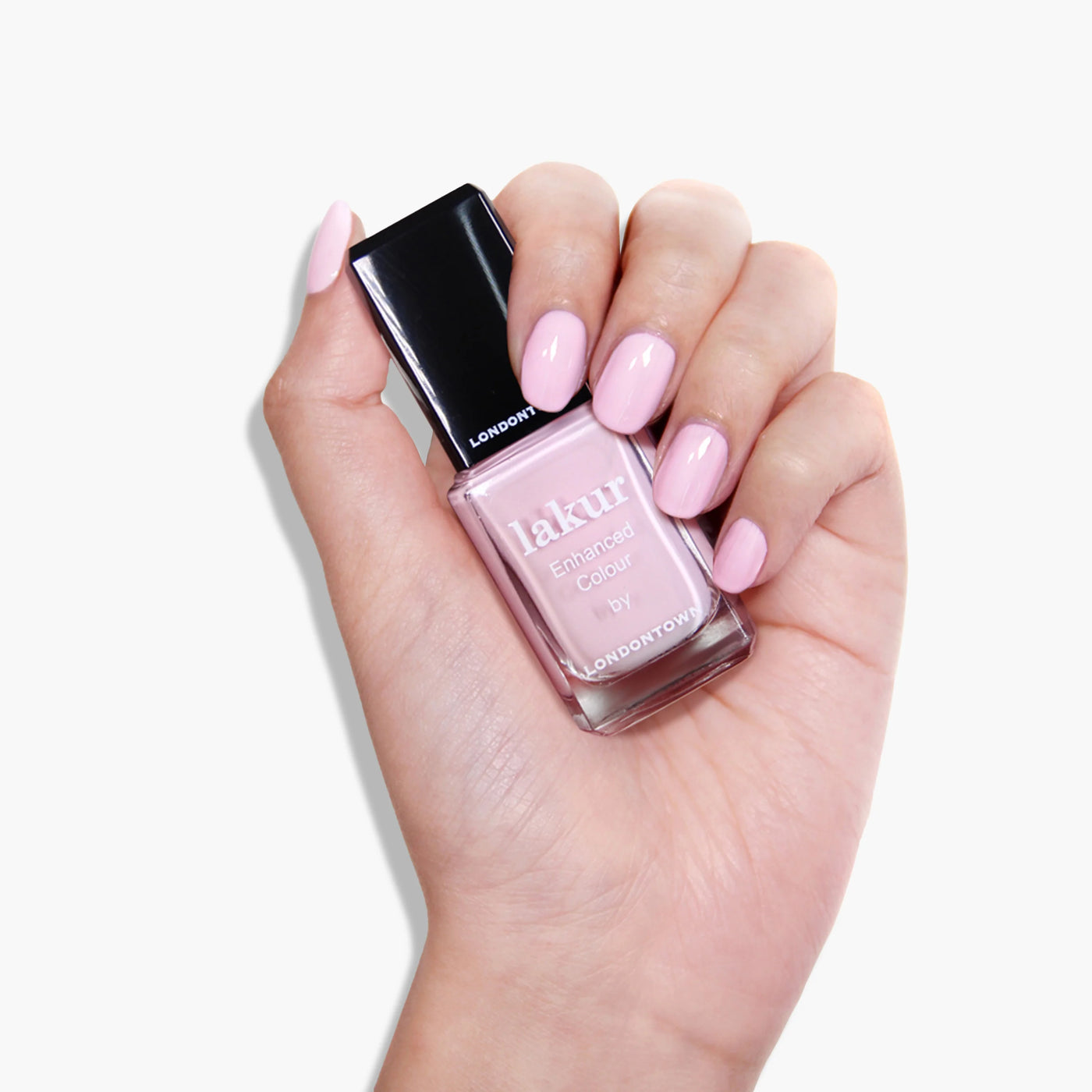 A hand holding a bottle of LONDONTOWN's Afternoon Tea (Professional) nail polish in a light pink crème shade, perfect for those warm and cozy moments with a cup of tea.