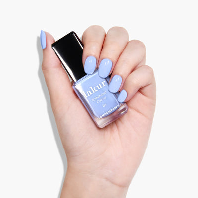 Hand holding a bottle of LONDONTOWN's Amalfi Love (Professional) nail polish against a white background. Fingernails are painted in the same light blue color, exuding beach vibes. The polish features the Florium Complex and is vegan cruelty-free.