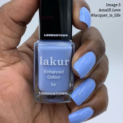 A hand holds a bottle of Londontown's Amalfi Love (Professional) nail polish, featuring a light blue shade infused with the nourishing Florium Complex. The painted nails exude beach vibes. Text on the side reads "Image 3 Amalfi Love @lacquer_is_life.