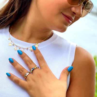 A person wearing aviator sunglasses, a white sleeveless top, a butterfly necklace, and several rings shows off their neon blue manicured nails with LONDONTOWN's Cabana Boy (Professional).