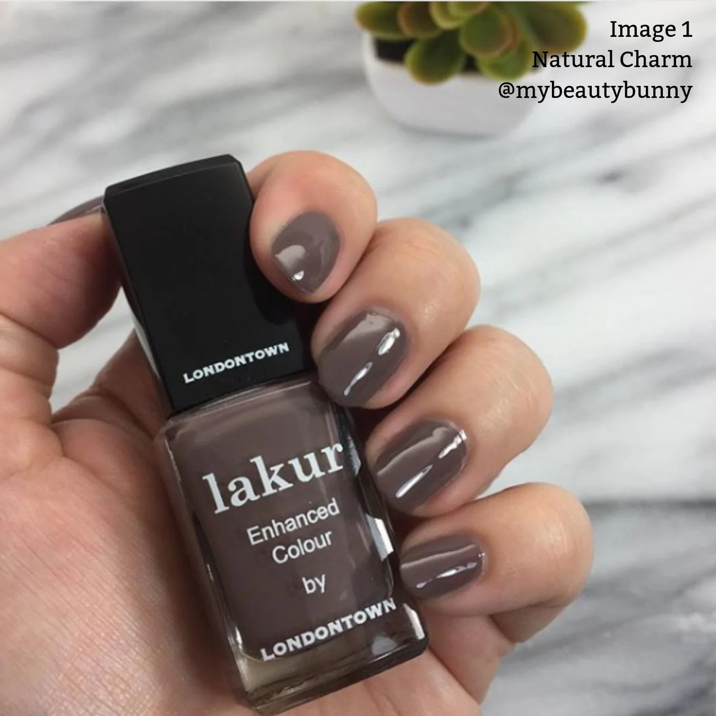 Person's hand with gray nail polish holding a bottle of Natural Charm (Professional) by LONDONTOWN, featuring their Florium Complex for healthy nails, with a small potted succulent in the background. Text reads: "Image 1 Natural Charm @mybeautybunny".